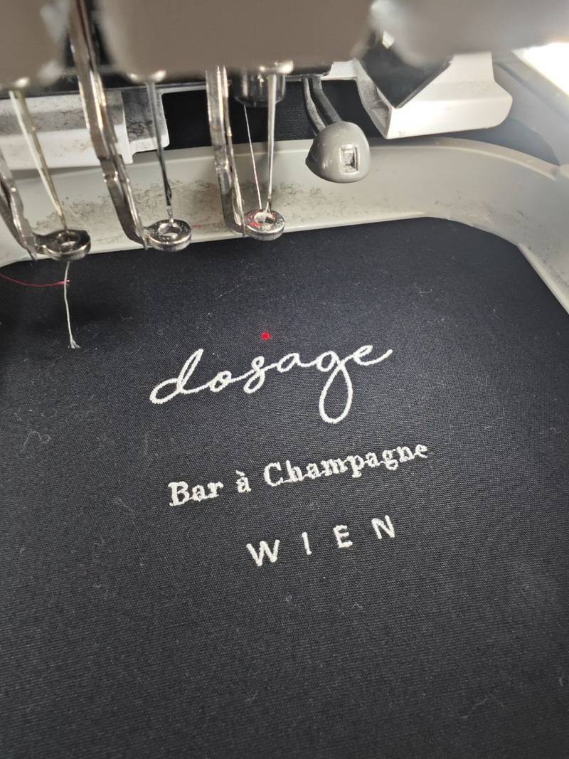 Dosage Bar à Champagne Wien, Feine weiße Stickerei auf schwarzem Stoff