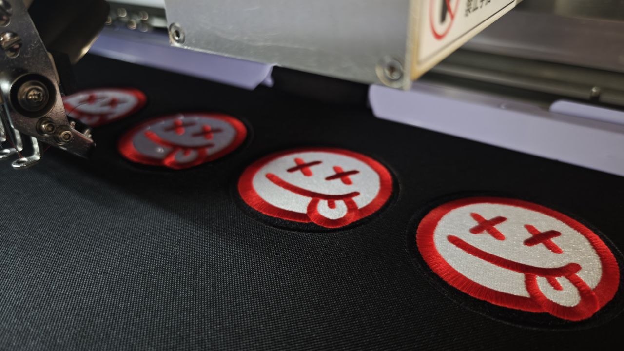 Aufnäher mit roten Smileys auf schwarzem Stoff unter dem Stickkopf